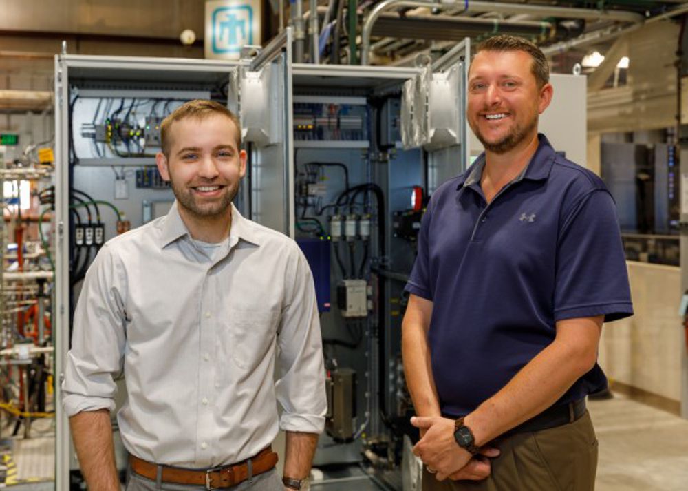 Logan Rapp (left) and Darryn Fleming, Sandia National Laboratories mechanical engineers, stand with the control system for the supercritical carbon dioxide Brayton cycle test loop. Earlier this year, the engineers delivered electricity produced by this system to the grid for the first time. Photo by Bret Latter/Sandia National Laboratories